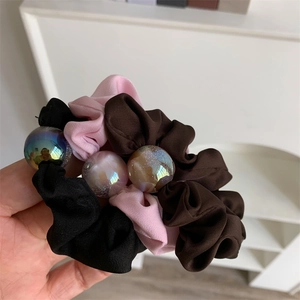 Close-up of elegant satin scrunchies in black, pink, and brown with iridescent bead charms