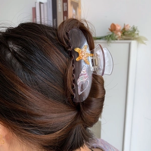 Detail view of purple acetate shark hair claw clip with golden starfish worn on hair
