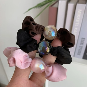 Close-up of satin scrunchies in brown, black and pink with shimmering iridescent beads
