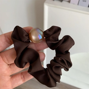 Close-up of a brown satin scrunchie with a large iridescent amber pearl detail
