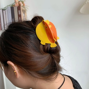Détail d'une pince à cheveux poisson jaune et orange portée sur un chignon