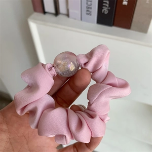 Pink silky scrunchie with a transparent sequin ball charm shown on a hand