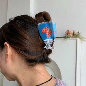 Detail of blue acetate hair claw clip with red crab motif worn on long brown hair