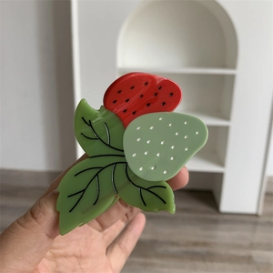Détail de la pince à cheveux fraise en acétate montrant les textures rouge et verte des feuilles