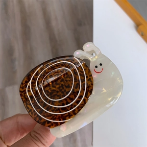 Détail de la pince à cheveux en acétate en forme d'escargot avec motif écaille et smiley