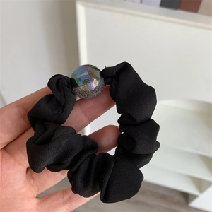 Detailed view of a black ruffled fabric hair scrunchie featuring a glittery resin orb charm