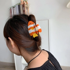 Détail macro d'une pince à cheveux poisson portée par un mannequin dans un intérieur