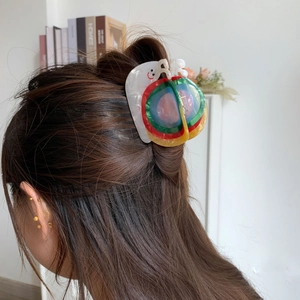 Gros plan d'une pince à cheveux en acétate arc-en-ciel portée sur une coiffure en queue