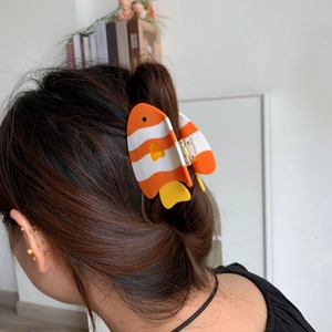 Détail d'une pince à cheveux en forme de poisson orange et blanc sur les cheveux d'un modèle