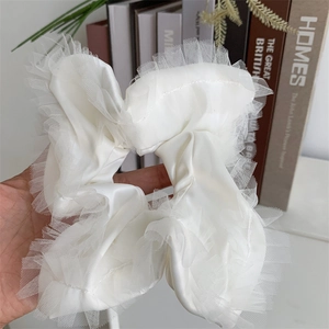 Detailed close-up of a white satin scrunchie featuring elegant lace trim and soft pleats