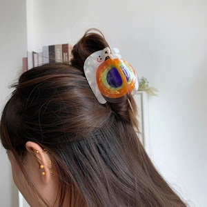 Détail d'une pince à cheveux en acétate en forme d'escargot avec un visage souriant sur cheveux