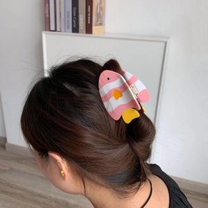 Détail d'une pince à cheveux en forme de poisson en acétate coloré sur un chignon