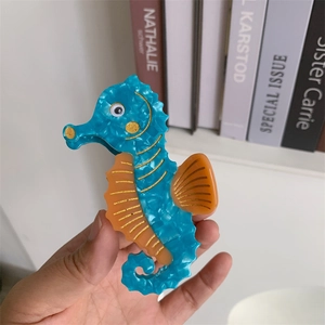 Detail of seahorse-shaped acetate hair claw with blue shimmer and orange fin accents