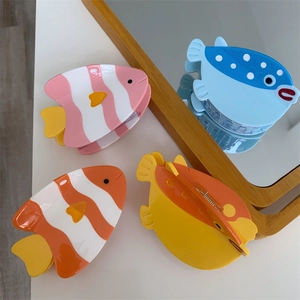 Détail de quatre pinces à cheveux en forme de poisson coloré en acétate sur table blanche