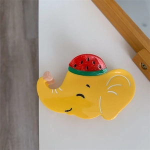 Détail de la pince à cheveux éléphant jaune avec chapeau rouge et breloque cœur rose