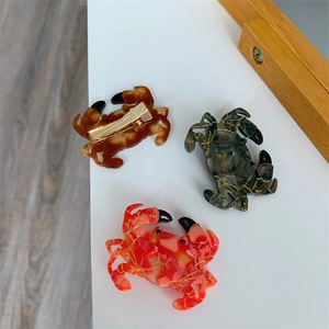 Détail de pinces à cheveux en forme de crabe, couleurs corail, vert et marron doré