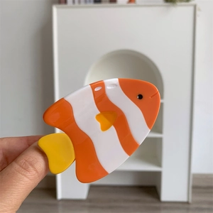Détail d'une pince à cheveux poisson-clown orange et blanc en acétate tenue en main