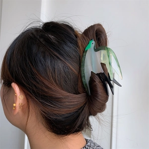 Détail de la pince à cheveux hirondelle en acétate vert sur un chignon brun foncé