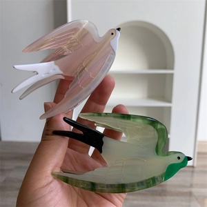 Détail de la main tenant des pinces à cheveux hirondelle en acétate dégradé rose et vert