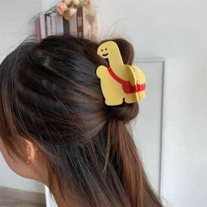 Détail d'une pince à cheveux dinosaure jaune avec sac rouge portée sur cheveux bruns