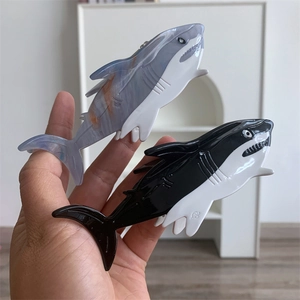 Detail showing marble grey-blue and glossy black shark-shaped hair claw clips being held