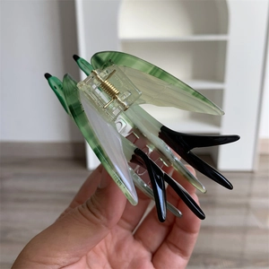 Détail d'une pince à cheveux hirondelle en acétate vert montrant le ressort dans la main