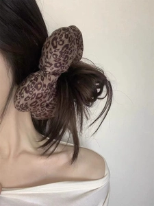 Detail of a large 3D stuffed leopard print bow hair tie worn on a woman's ponytail