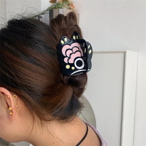 Detail view of a black acetate bear paw hair claw with colorful abstract fish patterns