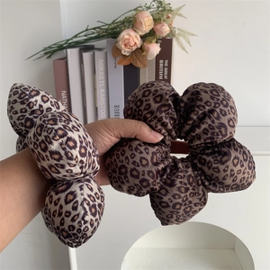 Detailed view of oversized leopard print satin flower scrunchies held in hand for scale