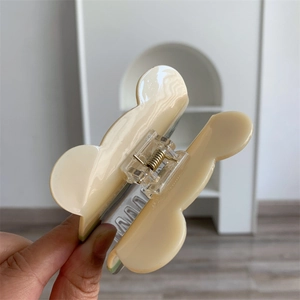 Detalle de la pinza para el pelo ondulada en color crema con un resorte de metal dorado