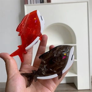 Mano che tiene fermagli per capelli a forma di balena in acetato rosso e tartarugato