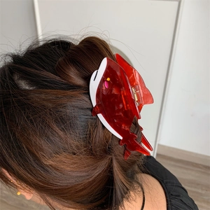 Dettaglio della molletta per capelli a forma di squalo rosso e bianco su capelli castani
