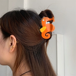 Detailopname van de oranje zeepaardje haarklem die een haarknot bij een model vastzet