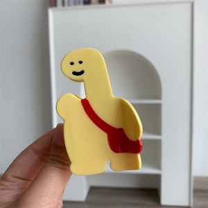 Détail d'une pince à cheveux girafe jaune avec un joli motif de petit sac à dos rouge