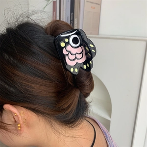 Detail view of a black monster eye hair claw clip with pink floral accents on a bun