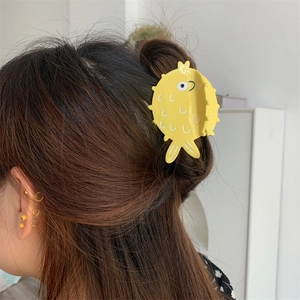 Close-up of a cute yellow pufferfish hair claw clip worn on a woman's dark ponytail
