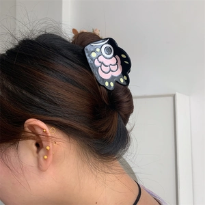 Detail view of a black claw clip with pink floral patterns on a messy hair bun style