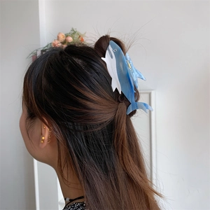 Detail view of the large blue shark-shaped acetate hair claw clip on a model's hair
