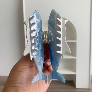 Detail showing hand holding a blue marble shark-shaped acetate hair claw with white teeth