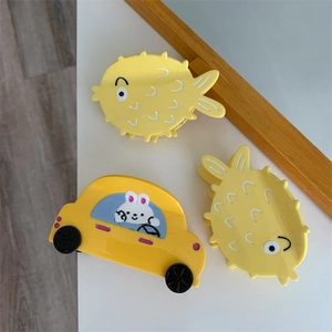 Close-up of yellow acetate hair claws in cute cartoon car and pufferfish shapes