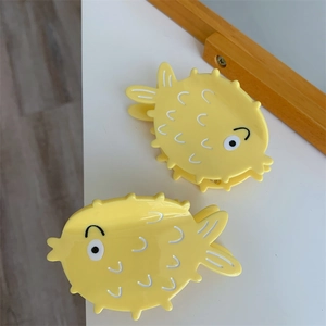 Detail of two cute yellow cartoon pufferfish hair claws made of glossy acetate material