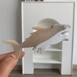 Close-up of shark shaped hair claw clip in beige acetate with detailed fin and teeth