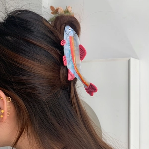 Detail shot of a pink fish-shaped acetate hair claw clip worn in a half-up hairstyle