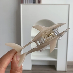 Detail shot of a cream beige acetate shark-shaped hair claw with strong gold spring