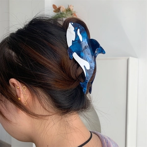 Detail of creative orca-shaped acetate hair claw clip worn on long dark brown wavy hair