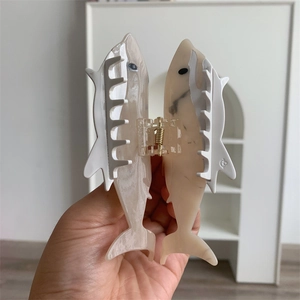 Detail of shark-shaped acetate hair claw with beige marble texture and metal spring
