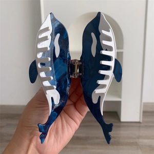 Detail of whale-shaped blue marble acetate hair claw clip held by hand for hair styling