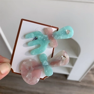 Dettaglio di fermagli per capelli in acetato marmorizzato verde menta e rosa a forma di posate