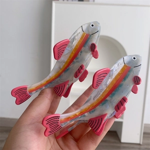 Detailed view of fish-shaped hair clips in pink and white acetate with vibrant stripes