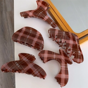 Detail showing various shapes of large brown and pink checkered hair claw clips on white surface